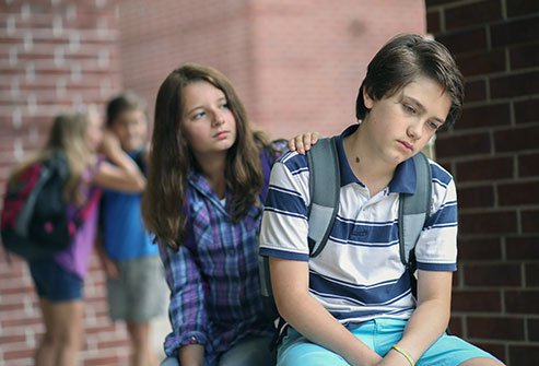 boy getting comforted by friend with bullies in the back