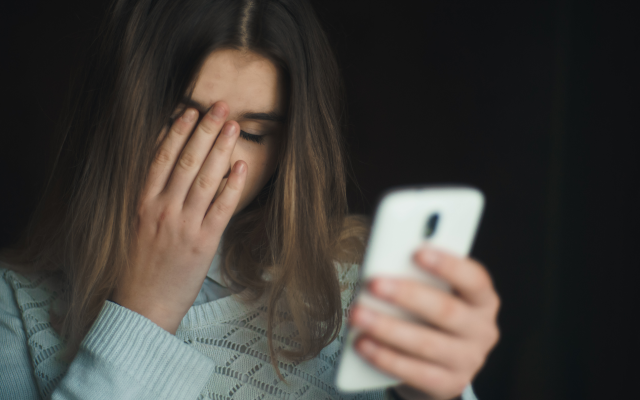 Girl holding her phone on one hand while covering her face with the other hand